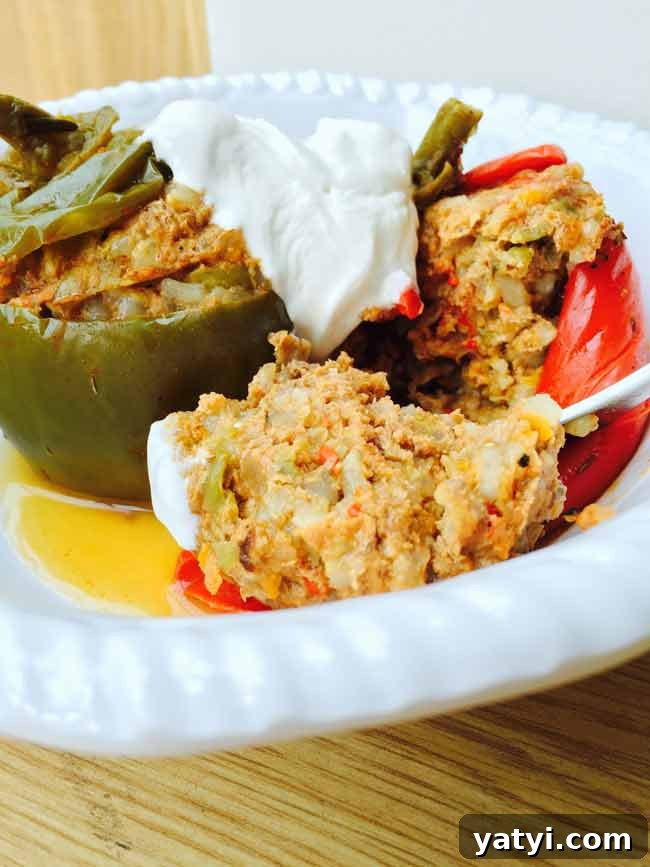 Stuffed Bell Peppers and Tomatoes Recipe for Summer Parties 3 A split stuffed pepper with cream topping, on a white plate and a spoon tucked in.