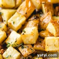 Crispy Garlic-Roasted Potatoes with Parmesan and Herbs 2 roasted potatoes on a baking sheet with thyme on top