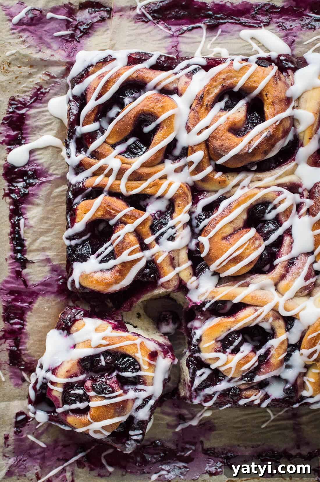 Citrus Lemon Blueberry Rolls (Vegan) 8 A top down shot of vegan lemon blueberry sweet rolls drizzled with lemon glaze on a sheet of baking parchment