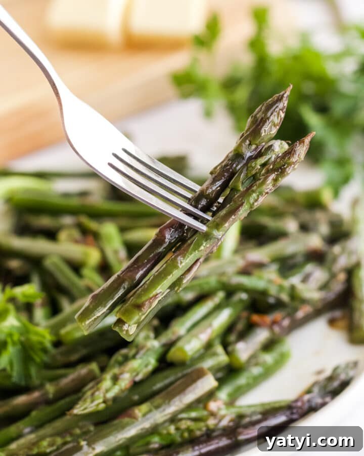fork holding bites of asparagus from a white plate