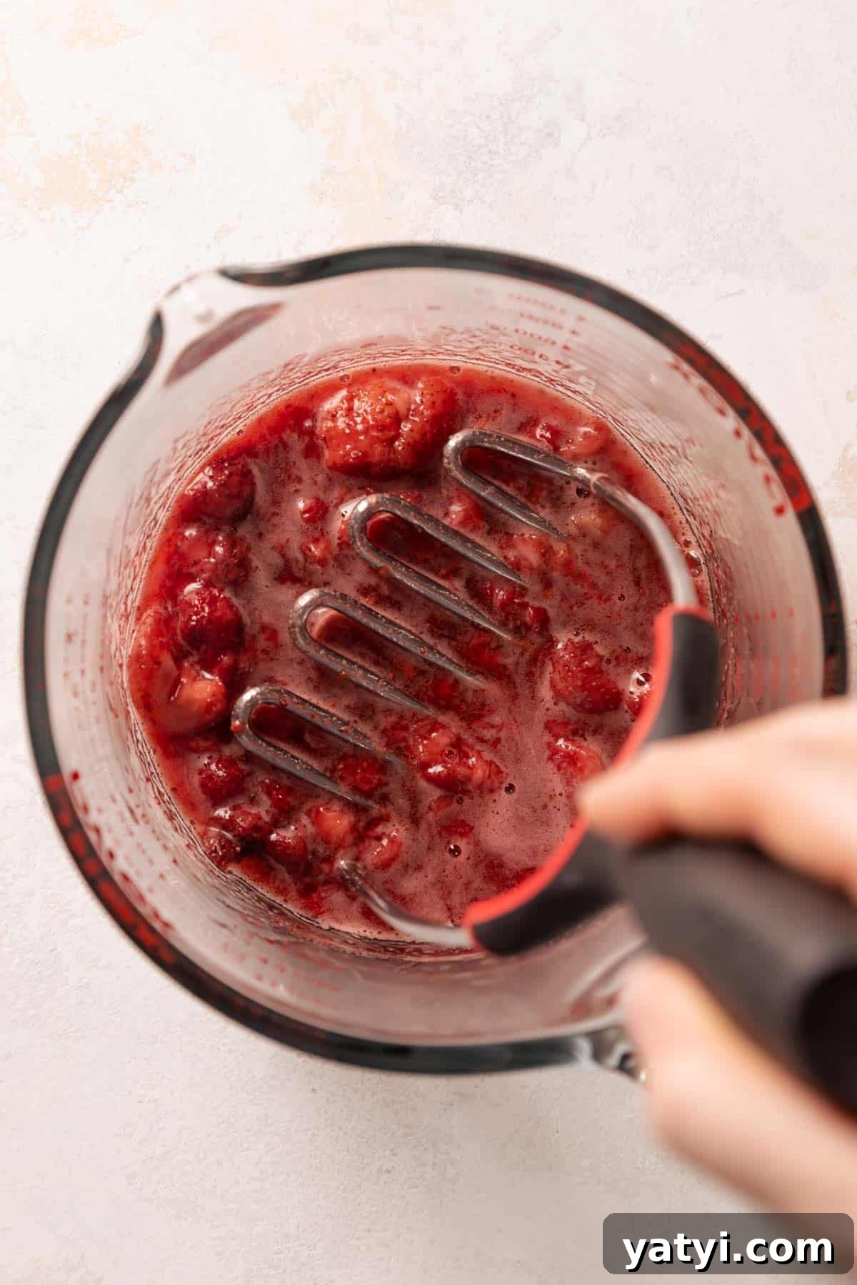 Strawberry Crunch Cupcakes Recipe with Crispy Topping 3 mashing roasted strawberries in a glass mixing bowl.