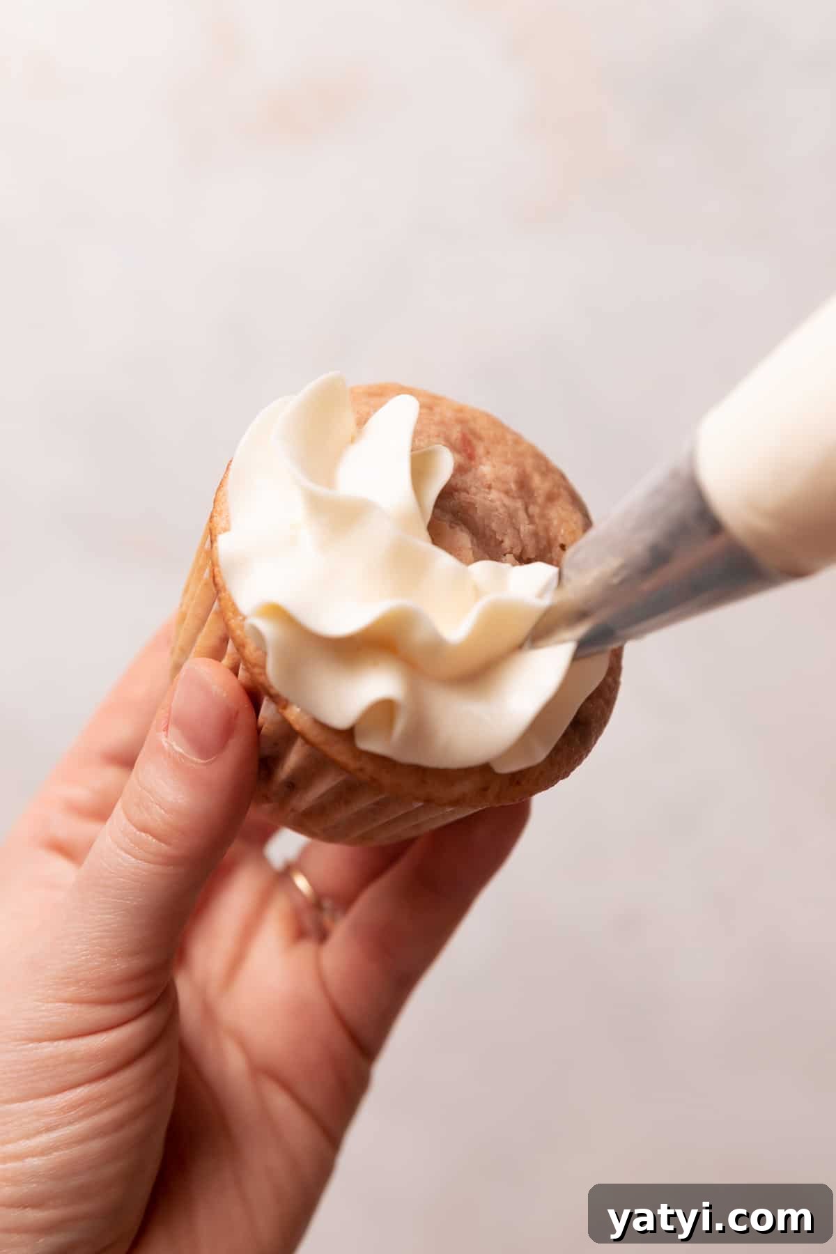 Strawberry Crunch Cupcakes Recipe with Crispy Topping 10 piping the vanilla frosting on top of a cupcake.