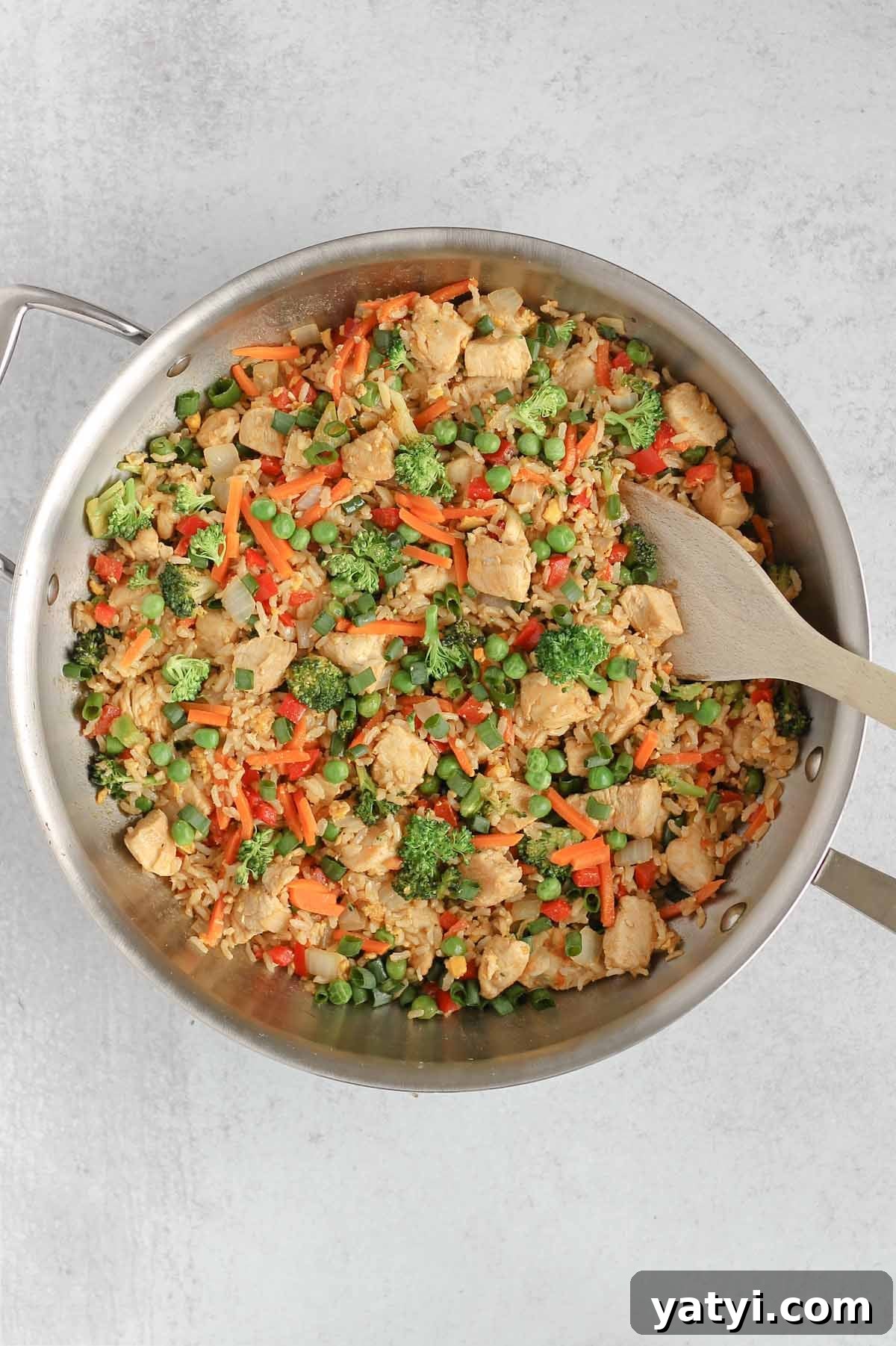 Low-Sodium Fried Rice Without Soy Sauce — Flavorful Vegetable Fried Rice 7 Chicken fried rice in a large cast iron skillet with a wooden spatula in the fried rice.