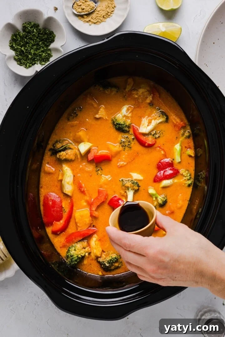 Slow Cooker Thai Red Curry with Chicken and Coconut Milk 7 Slow cooker thai-inspired red curry in a slow cooker, with a woman's hand pouring in soy sauce.