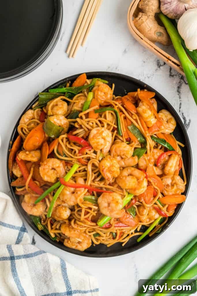 Garlic Shrimp Lo Mein Recipe — Quick Stir-Fry Noodles 2 Overhead view of shrimp lo mein on a black plate with shrimp, noodles, carrots, and green onions.