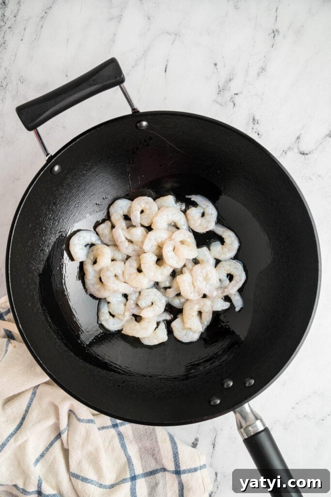 Garlic Shrimp Lo Mein Recipe — Quick Stir-Fry Noodles 6 Raw shrimp in a black wok with oil, beginning to cook for shrimp lo mein.