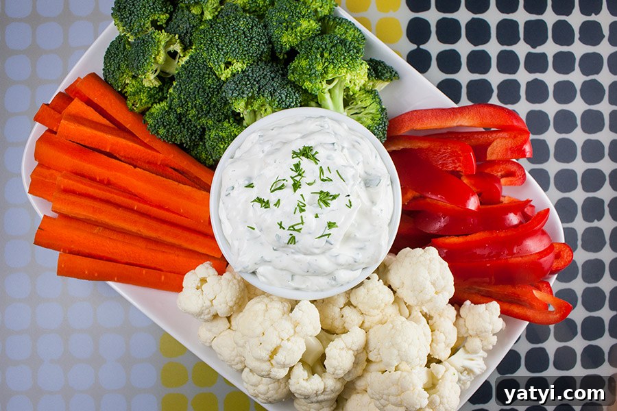 Fresh Herb Veggie Dip Recipe for Parties and Snacks 4 Fresh Herb Vegetable Dip in a white bowl surrounded by cut broccoli, cauliflower, carrots, and red bell peppers.