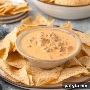 Creamy Velveeta Sausage Dip Recipe for Parties and Game Day 11 A bowl of creamy cheese dip with sausage and diced tomatoes in a small bowl on a large plate, accompanied by a plate of tortilla chips.