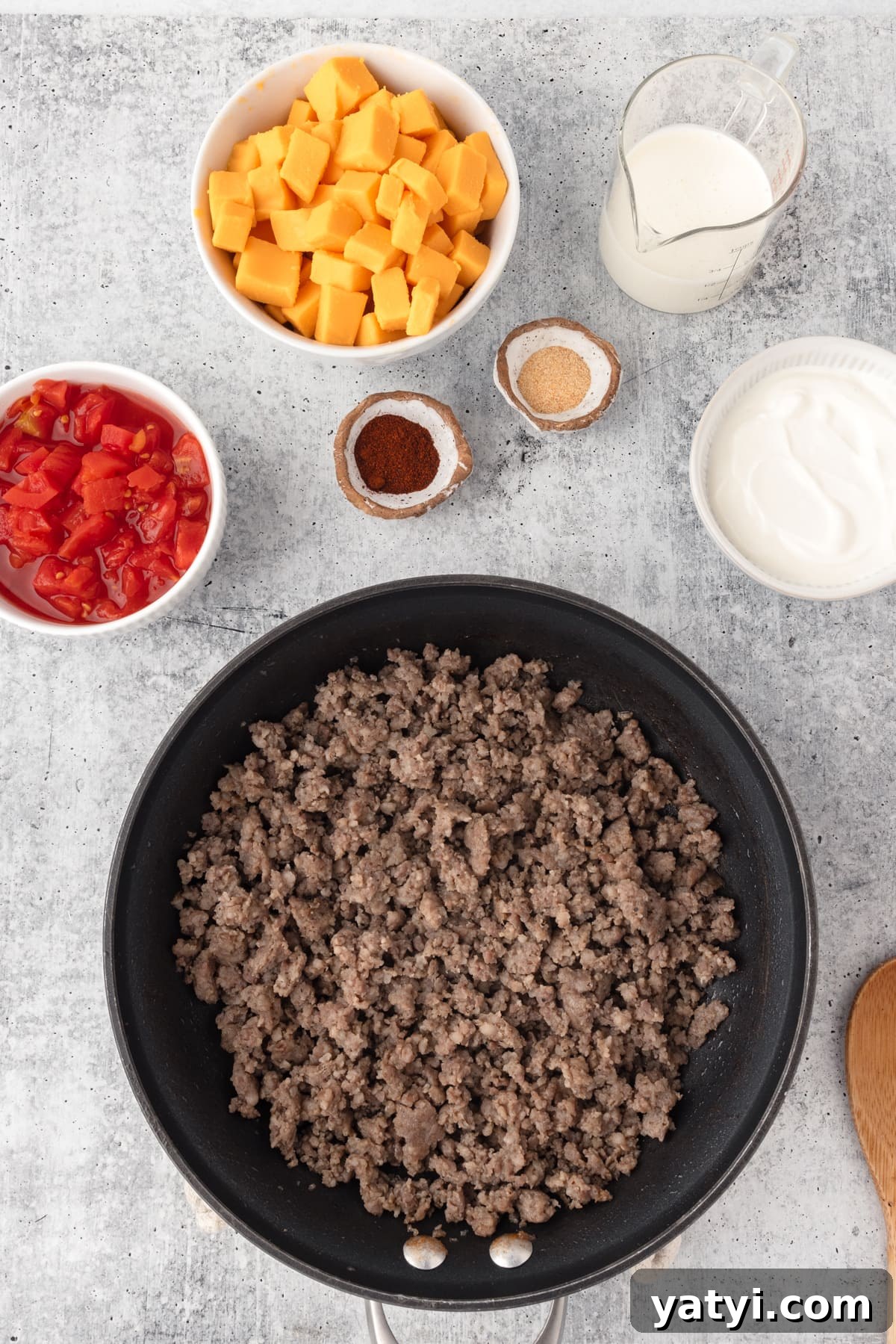 Creamy Velveeta Sausage Dip Recipe for Parties and Game Day 5 Velveeta Sausage Cheese Dip process shot shown. cooked sausgae in a black skillet with cubed cheese and tomatoes, seasonings on the side.