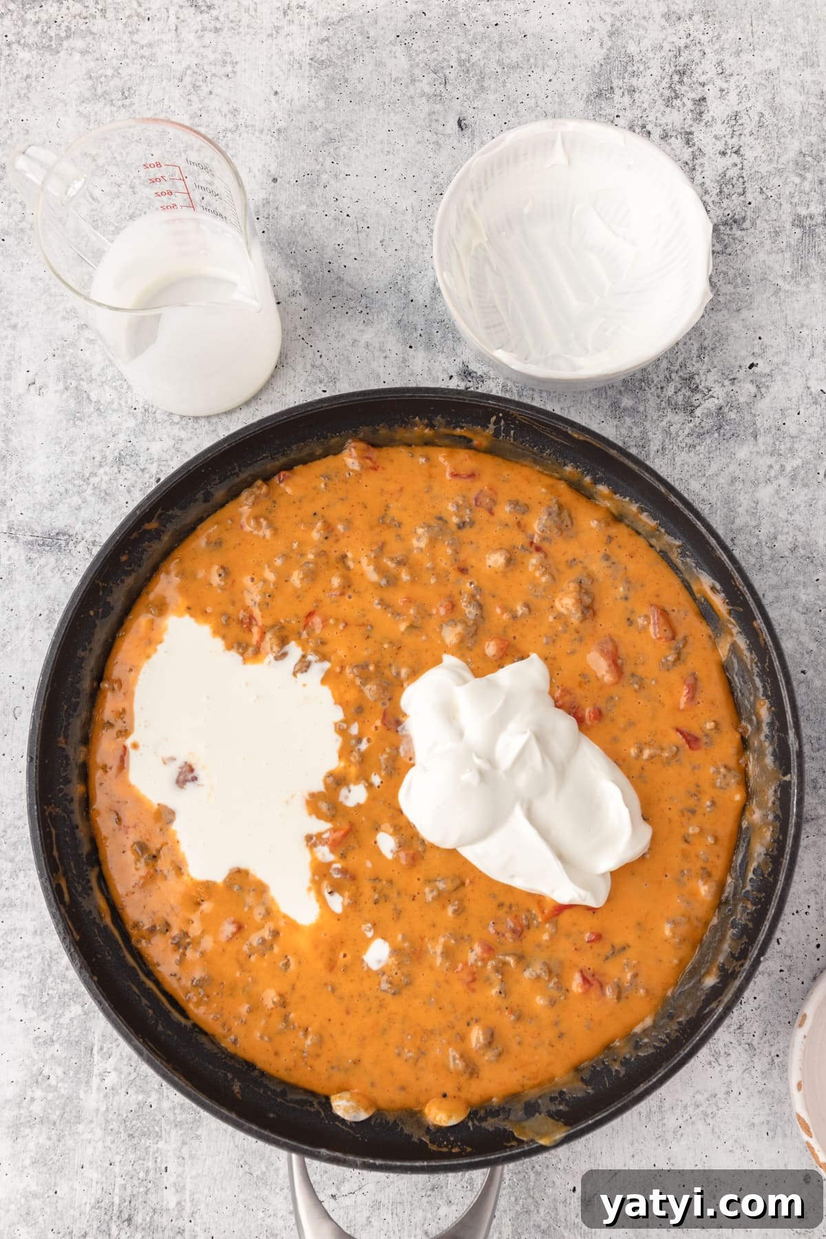 Creamy Velveeta Sausage Dip Recipe for Parties and Game Day 7 adding in sour cream into the velveeta cheese dip that's melted in a black skillet.