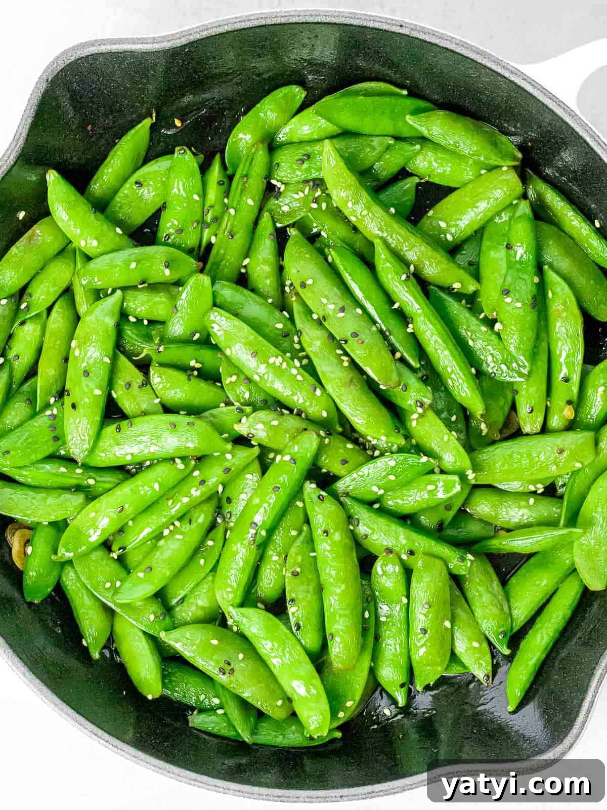Asian style sugar snap peas with garlic and black and white sesame seeds in a dark pan.