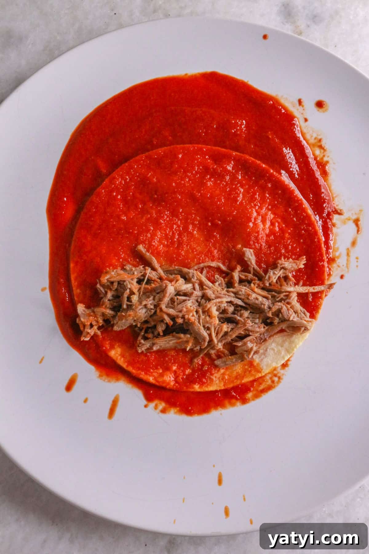Assembling an enchilada on a plate with shredded beef