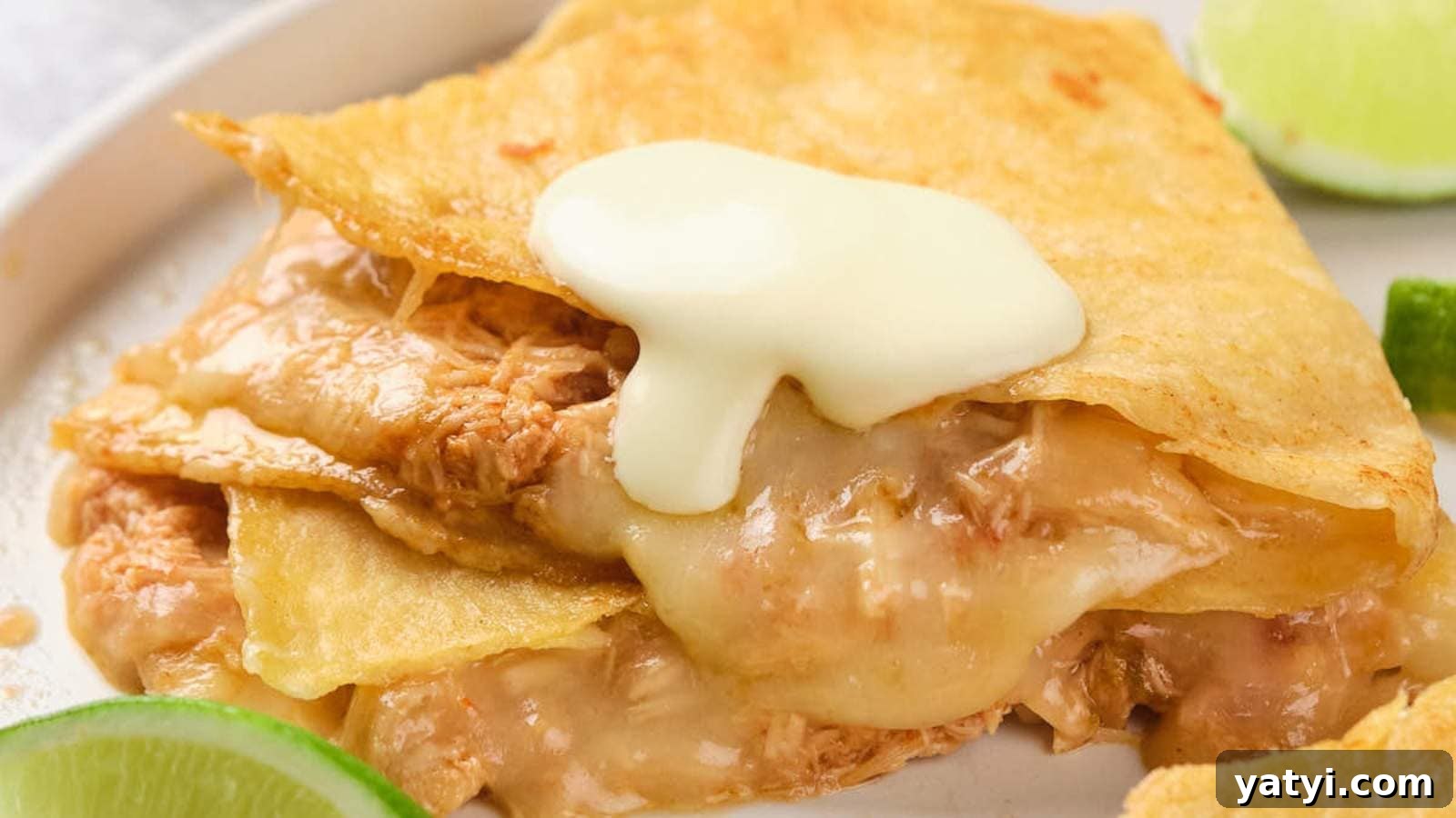 21 Snack Swaps That Beat Junk Food Without Sacrificing Flavor 2 Close-up of a cheesy quesadilla filled with shredded chicken, topped with cream, and served with lime wedges on the side.