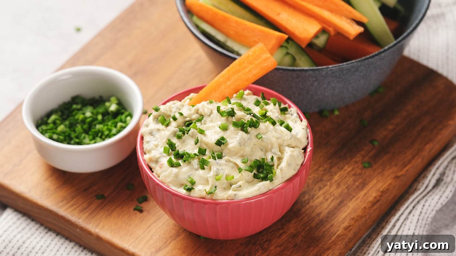 21 Snack Swaps That Beat Junk Food Without Sacrificing Flavor 12 A bowl of sour cream dip garnished with chopped chives, accompanied by carrot and cucumber sticks in a bowl.