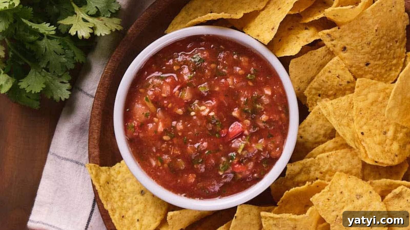 21 Snack Swaps That Beat Junk Food Without Sacrificing Flavor 3 A white bowl of salsa surrounded by tortilla chips on a wooden platter, with a sprig of cilantro nearby.