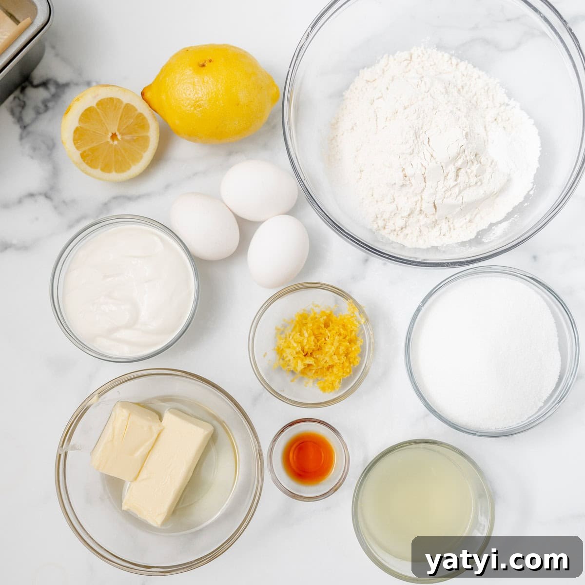 Copycat Starbucks Lemon Loaf Recipe: Moist Citrus Pound Cake Tutorial 3 Top-down view of baking ingredients on a white surface, including flour, sugar, eggs, sour cream, butter, vanilla, lemon juice, lemon zest, and a whole and halved lemon.
