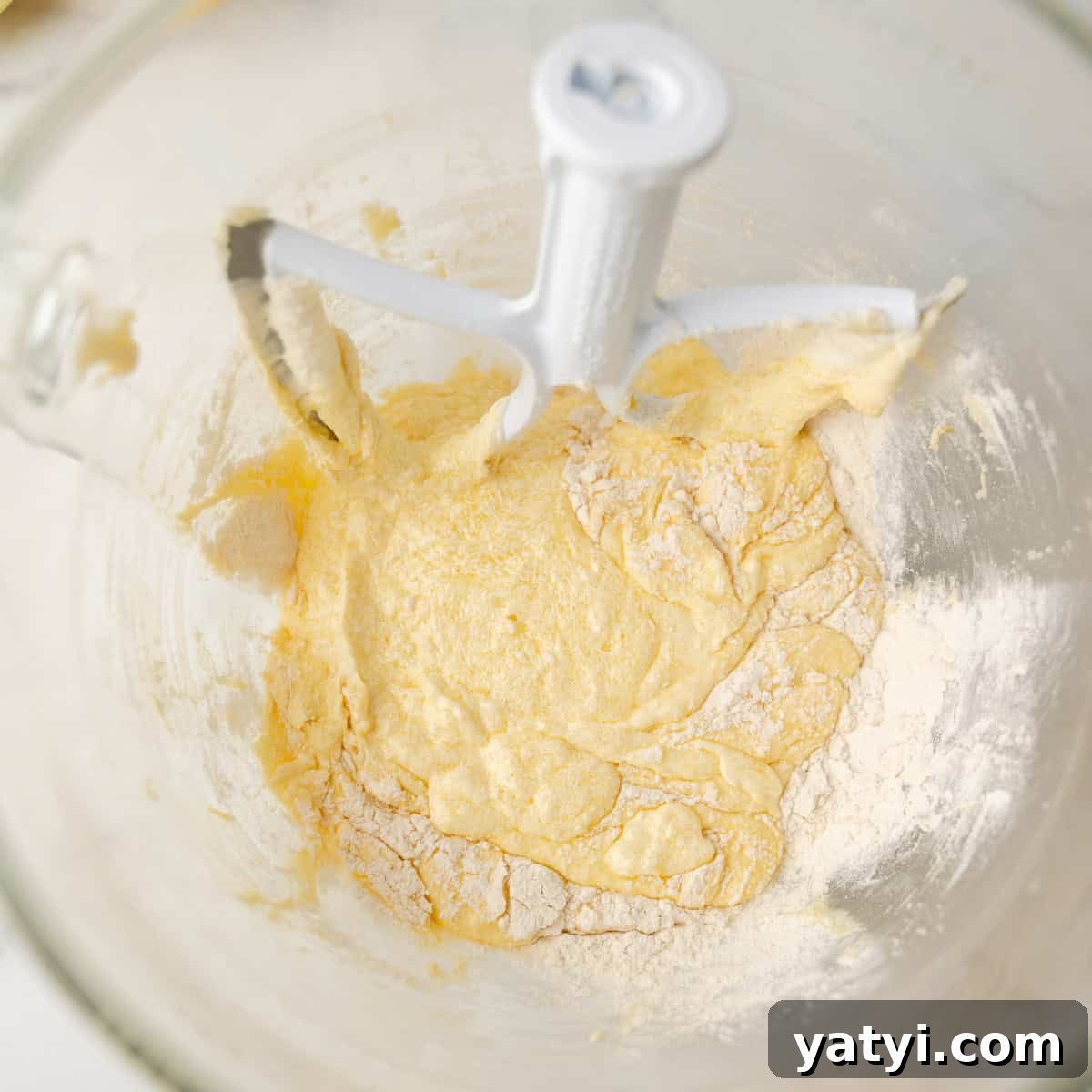 Copycat Starbucks Lemon Loaf Recipe: Moist Citrus Pound Cake Tutorial 5 A mixing bowl with a paddle attachment contains partially mixed yellow batter and flour.