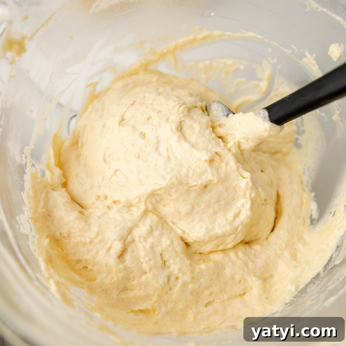 Copycat Starbucks Lemon Loaf Recipe: Moist Citrus Pound Cake Tutorial 6 A close-up view of thick, pale yellow cake batter being mixed in a glass bowl with a black spatula.