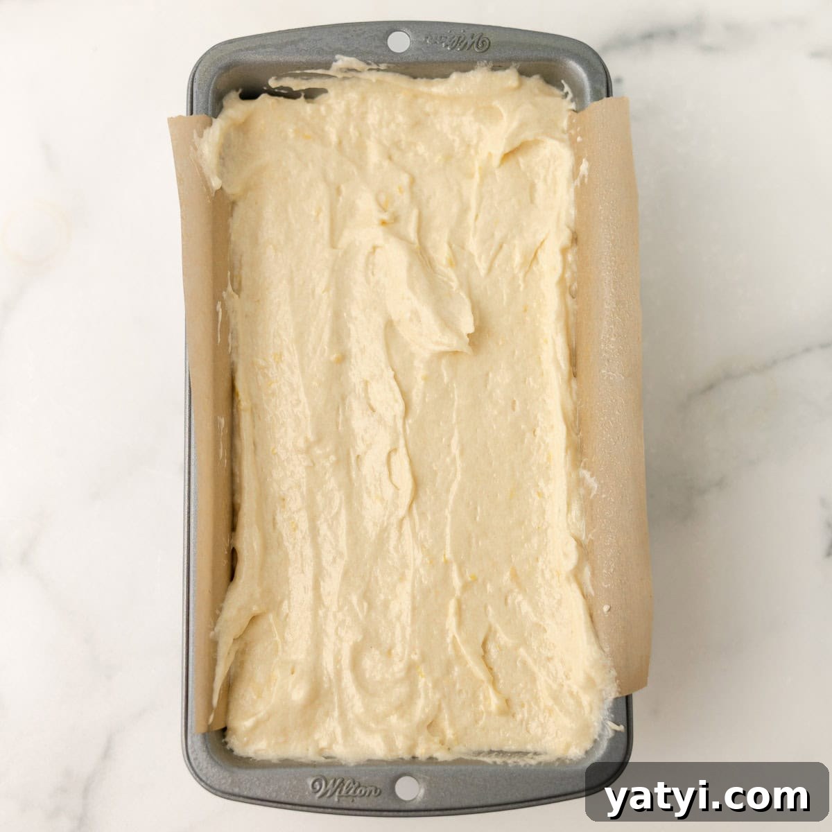 Copycat Starbucks Lemon Loaf Recipe: Moist Citrus Pound Cake Tutorial 7 A loaf pan lined with parchment paper is filled with unbaked batter, ready to be baked, on a light marble surface.