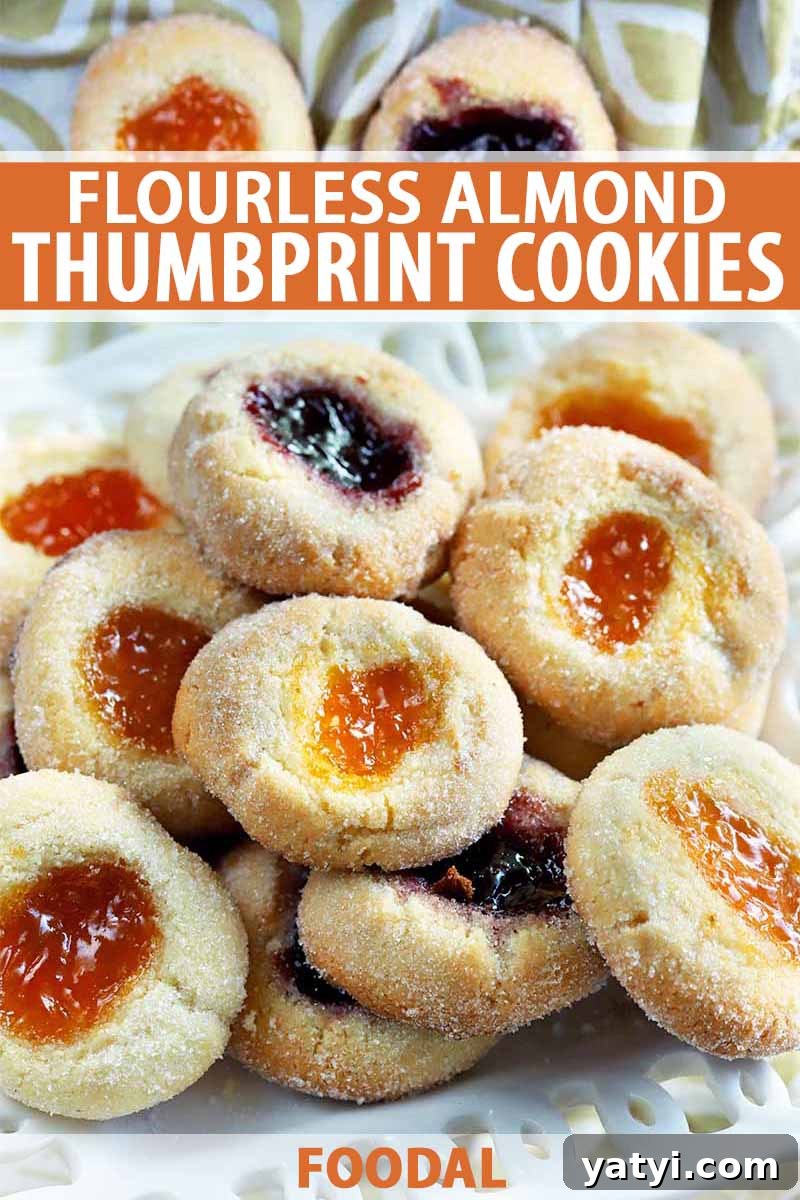 Vertical closeup of homemade almond thumbprint cookies filled with jam, arranged on a serving dish with a green and white cloth in the background, printed with orange and white text.
