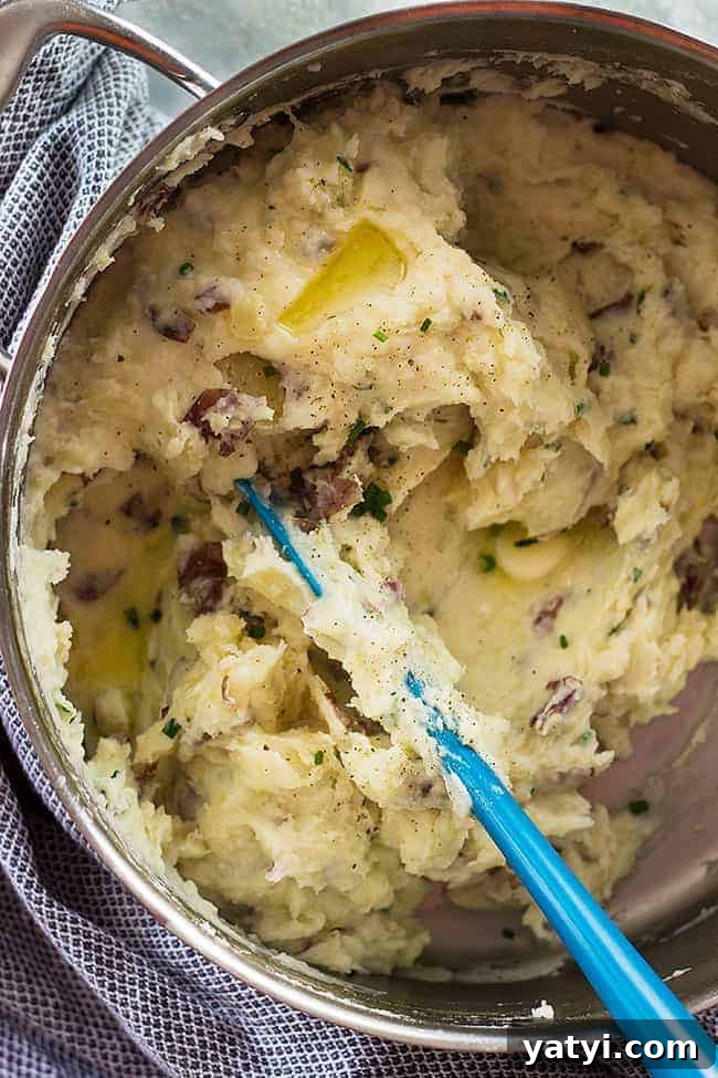 Creamy Chunky Mashed Potatoes with Rustic Texture 2 overhead closeup: a blue spatula stirring a big metal bowl of chunky mashed potatoes